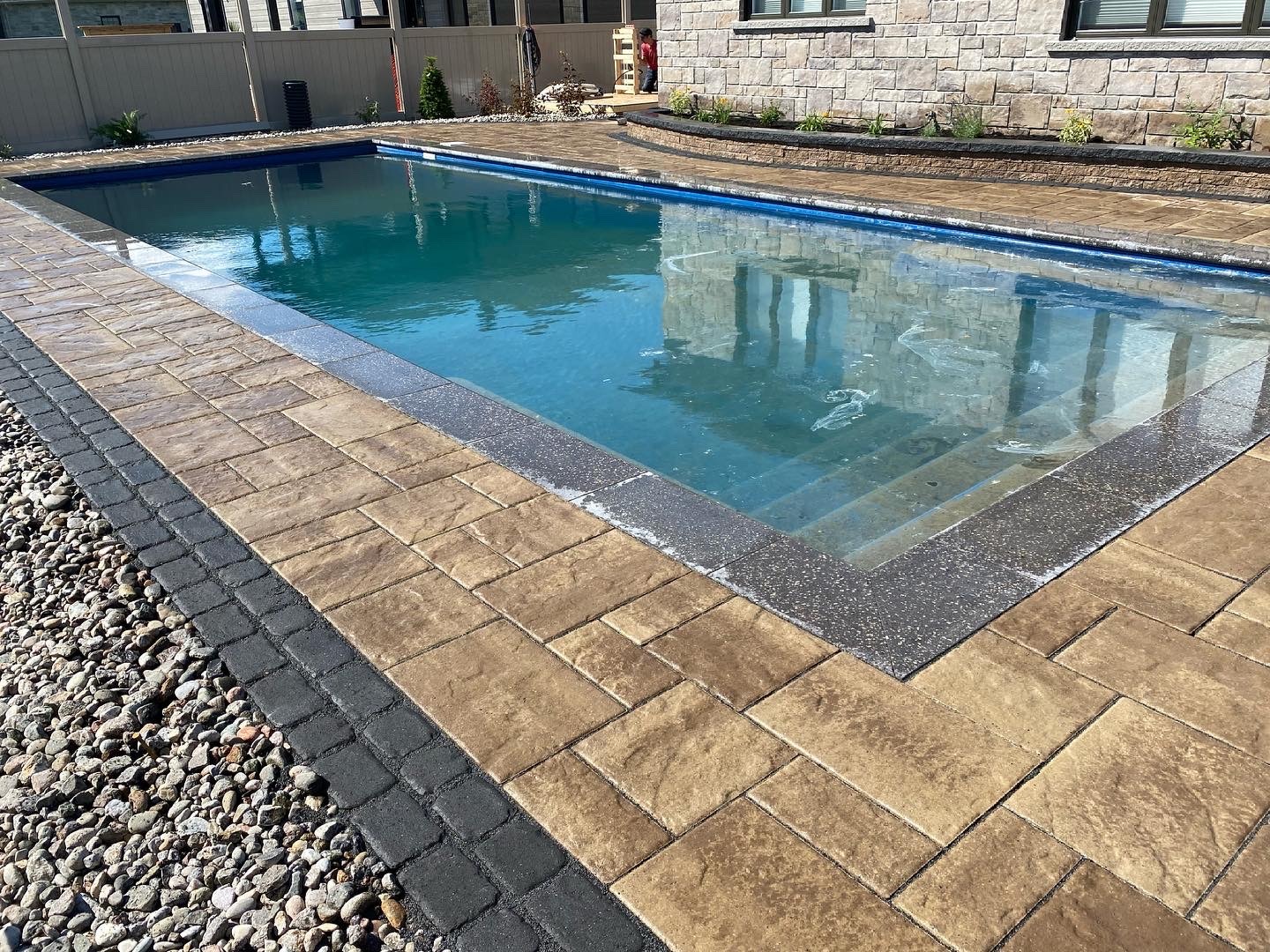 Backyard swimming pool with stone patio and wall.