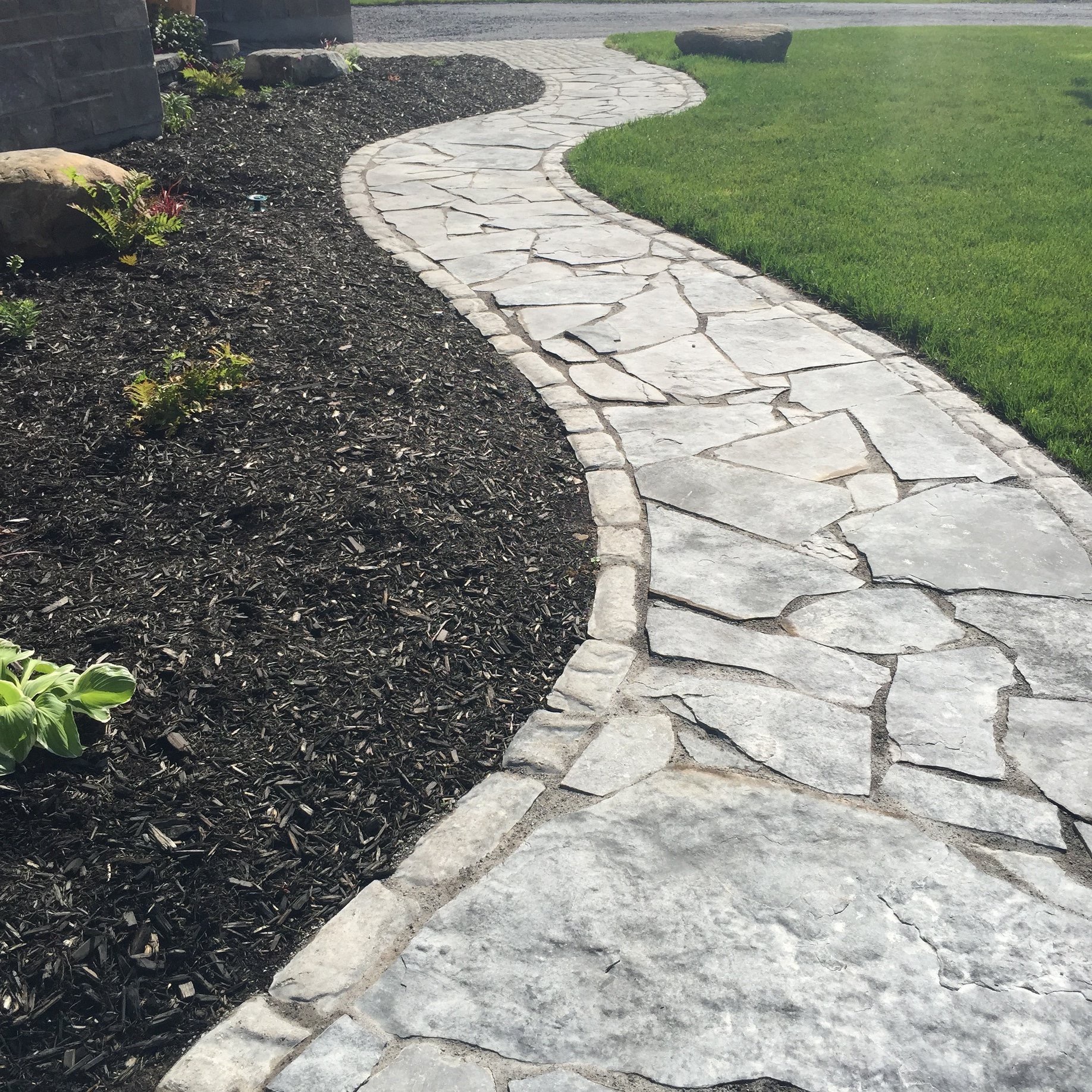 Curved stone pathway with surrounding mulch and grass.