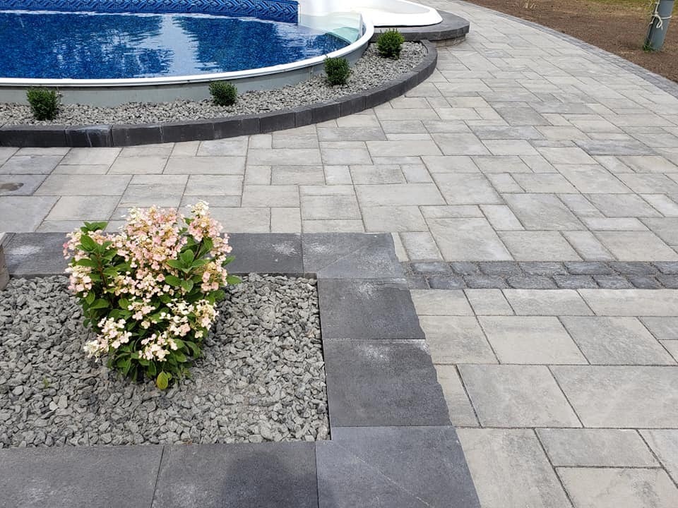 Paved patio with flowerbed and pool in background.