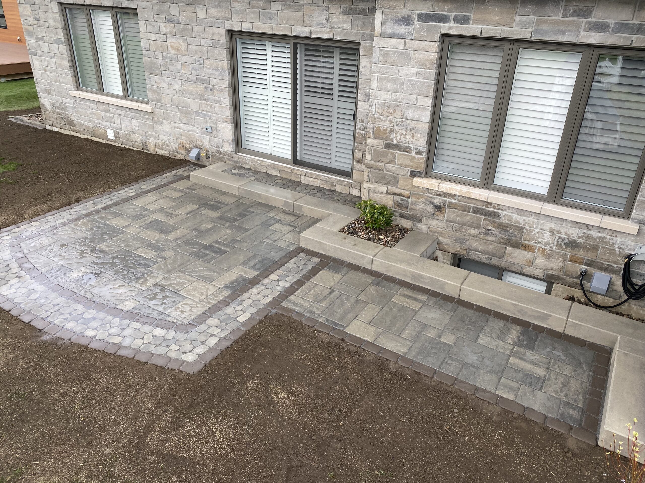 Newly tiled backyard patio next to stone house.