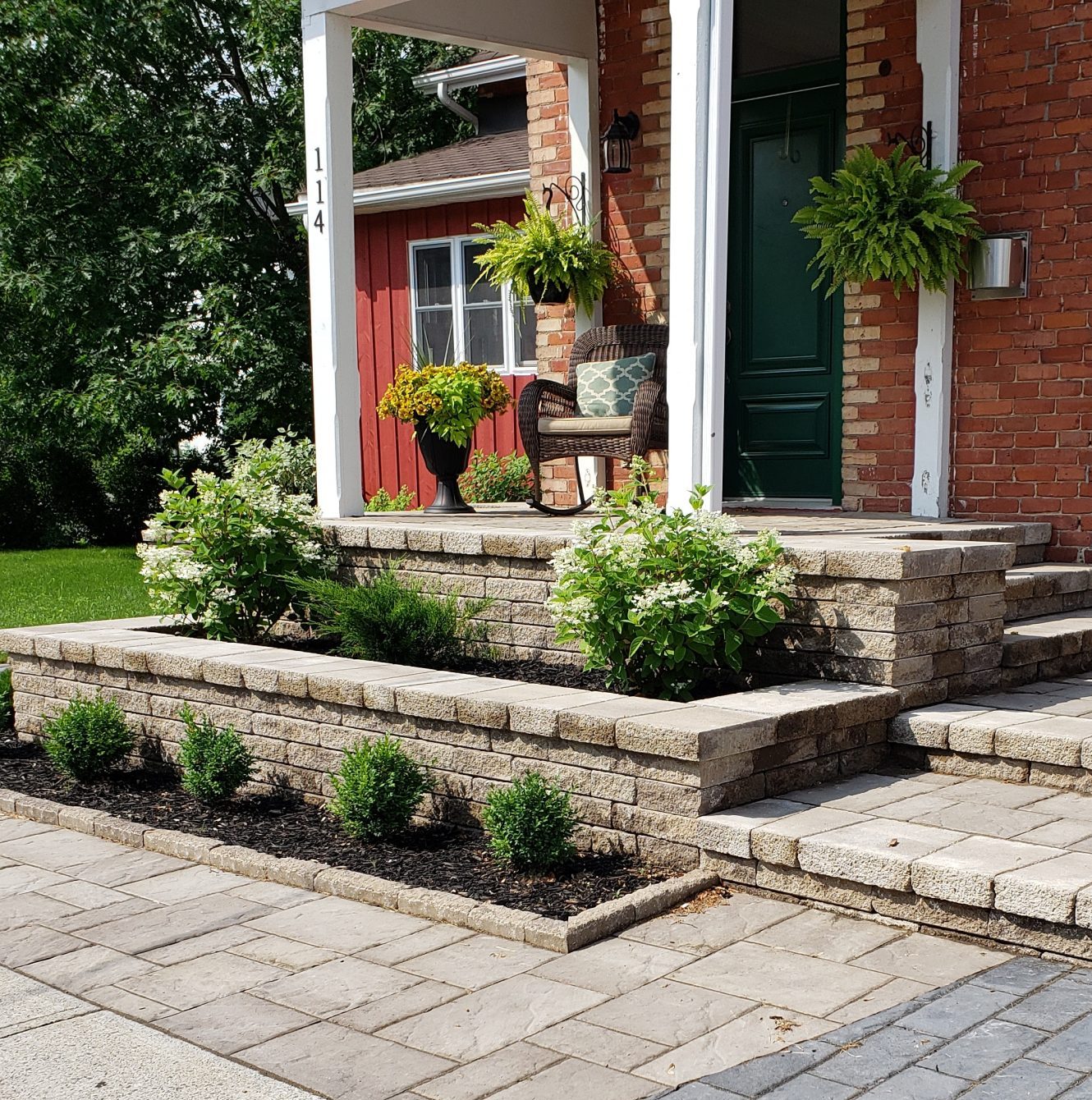 Brick porch with plants and wicker chair.