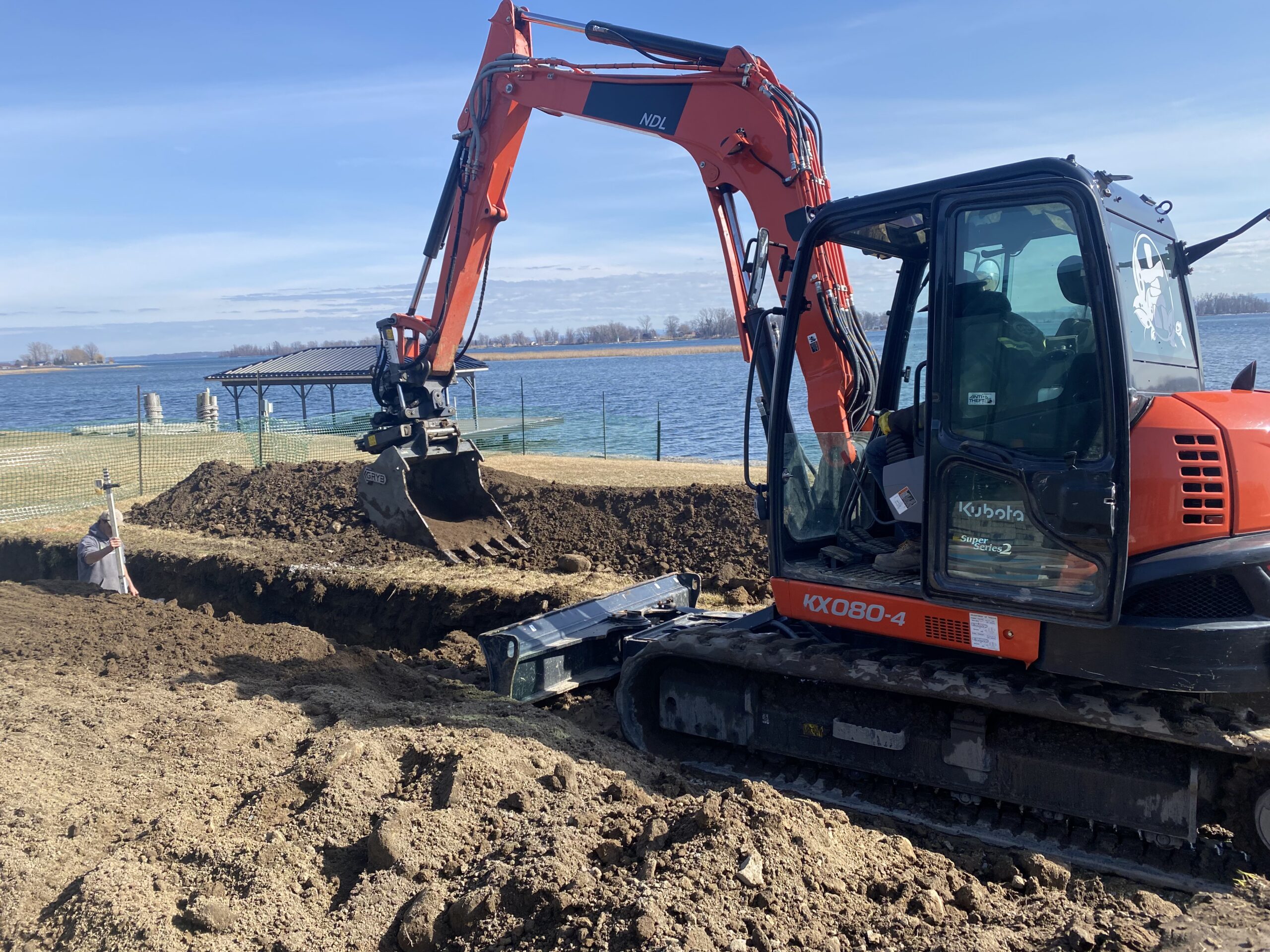 Excavator moving dirt near lakeside construction site.