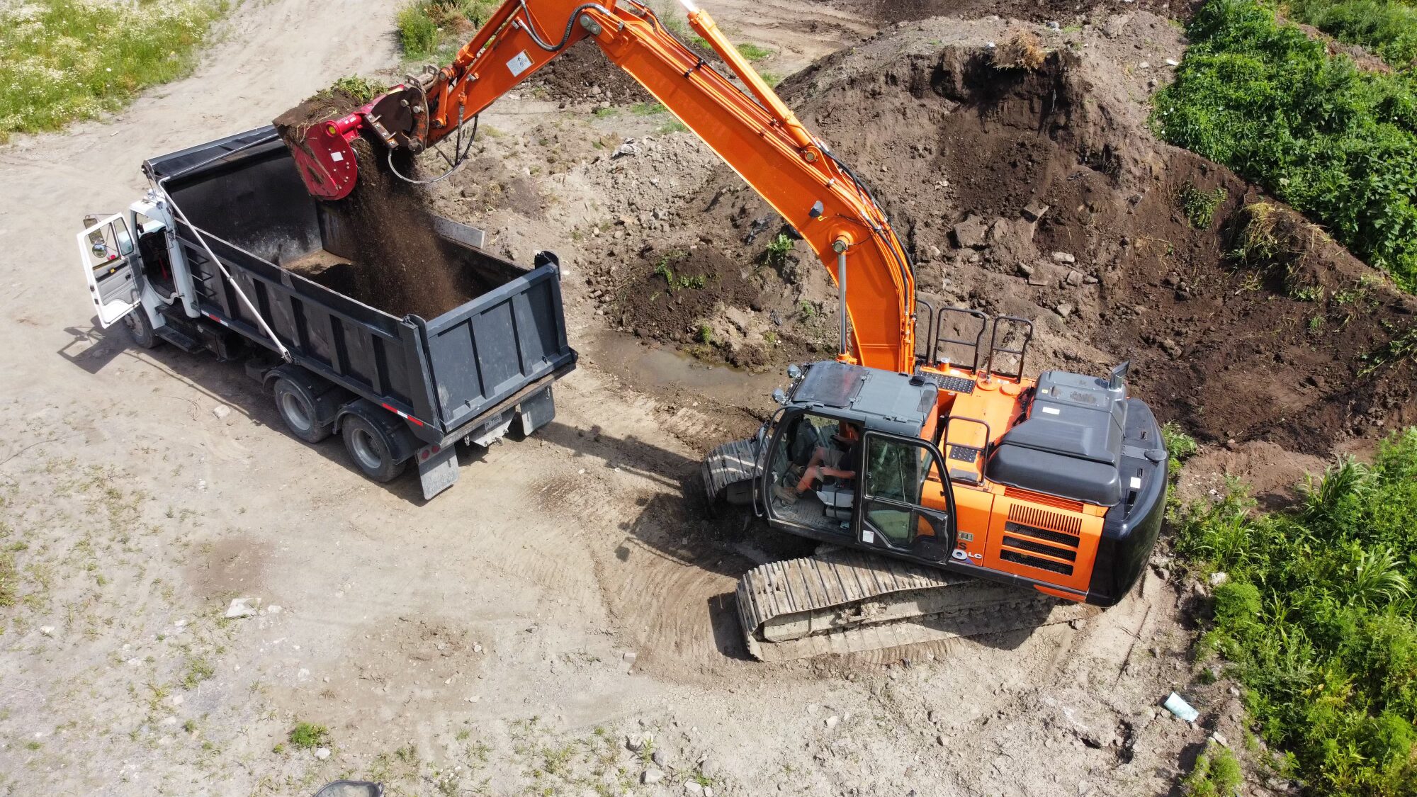 Excavator loading soil into dump truck at construction site.