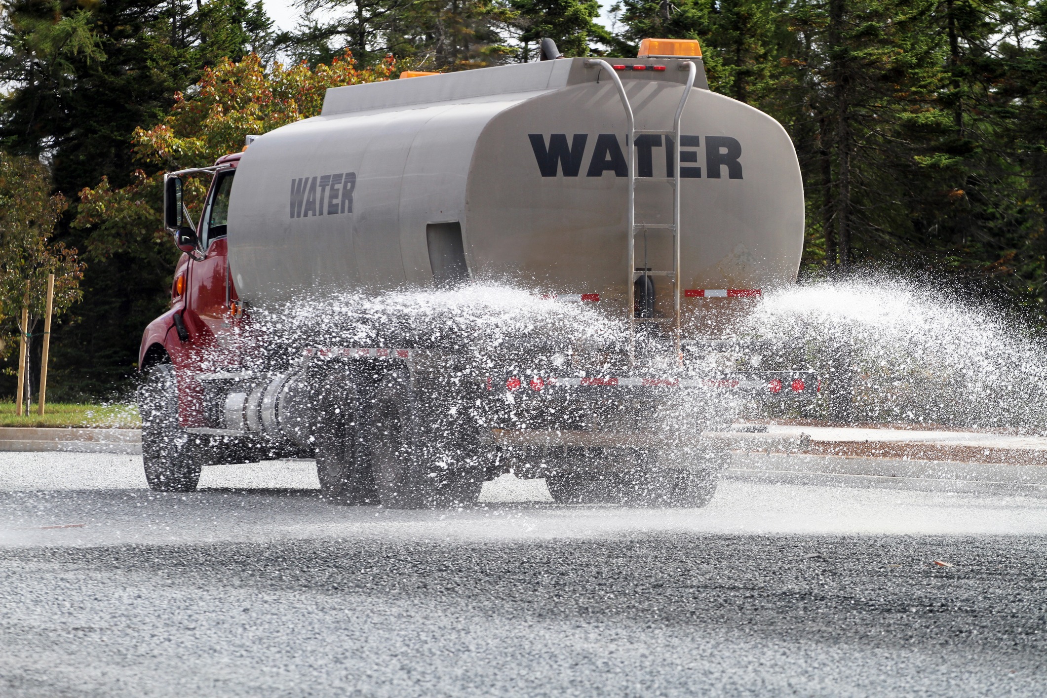 Water truck spraying gravel road in forest area.
