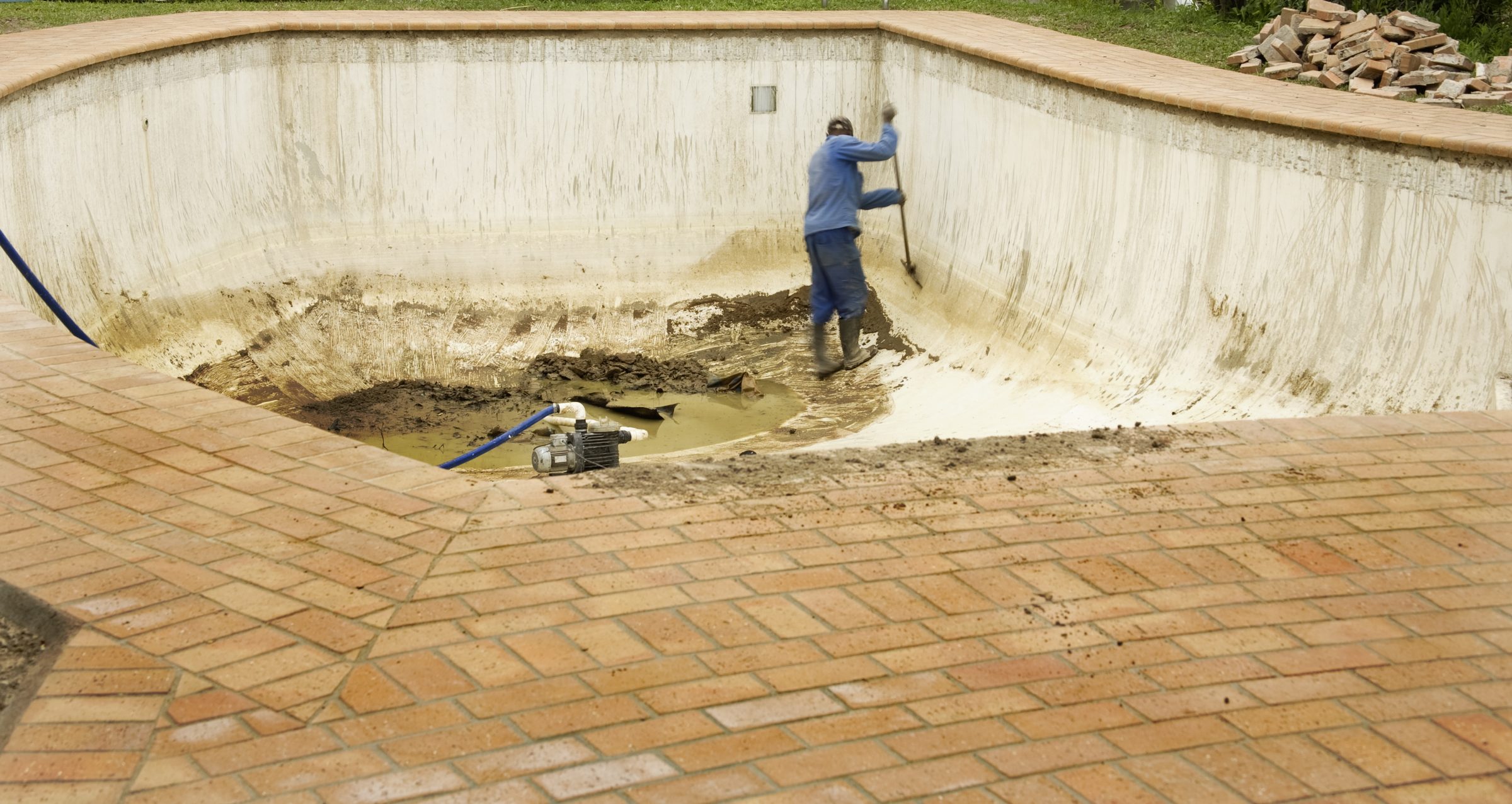 Worker cleaning empty swimming pool with hose.